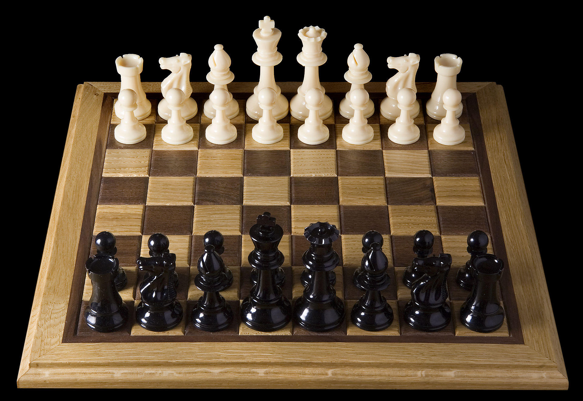 A staged walnut and boxwood chess set under dramatic light